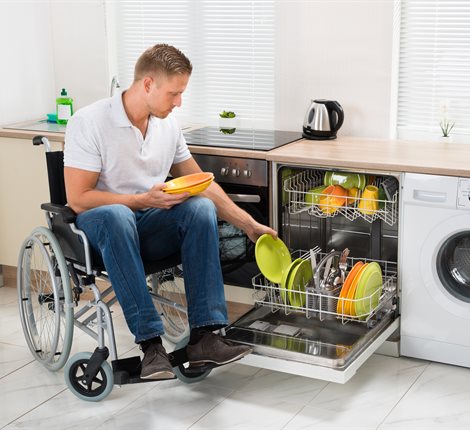 Man on a wheelchair using an accessible kitchen and loadiing a dishwasher