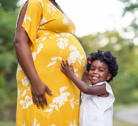Young girl smiling and holding her mum's pregnant tummy